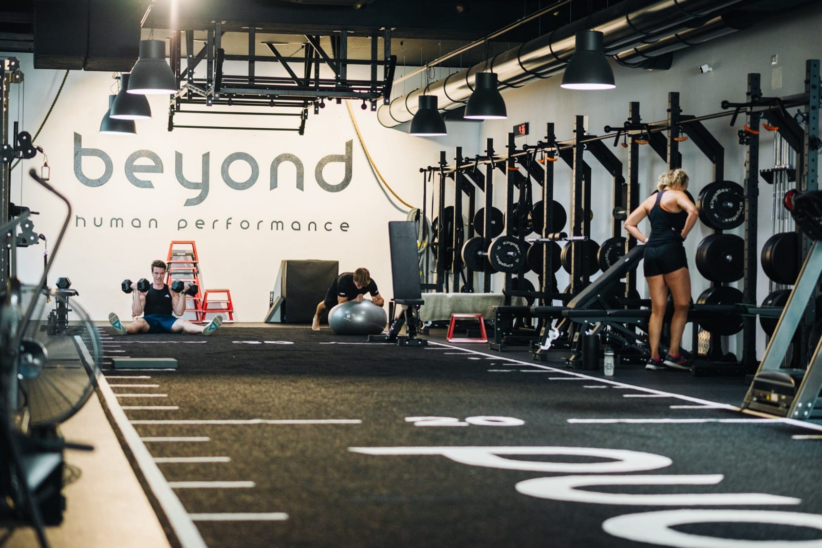 Open-Gym-Fläche bei beyond mit freien Gewichten, im Hintergrund trainieren zwei Personen eigenständig.